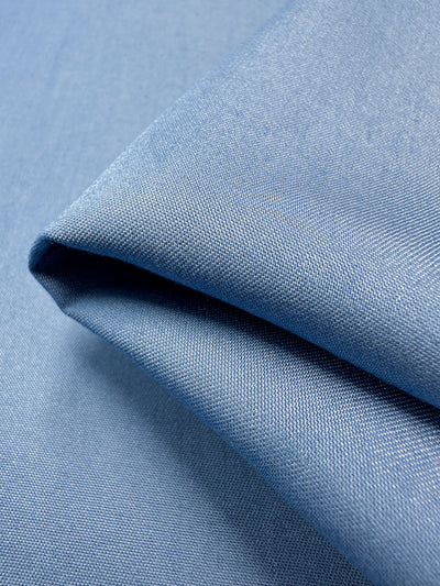 A close-up showcases a neatly folded piece of Super Cheap Fabrics' Chambray - Blissful Blue - 150cm, revealing its smooth texture and lightweight nature. The detailed view highlights the fabric's Chambray weave and soft appearance.