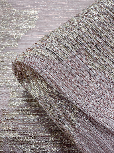 A close-up of a folded piece of Metallix Pleat fabric from Super Cheap Fabrics, featuring a shimmering and intricately woven textured polyester with a metallic gold and mauve pattern. Highlighted by hints of baby pink, this lightweight fabric appears soft and elegant.