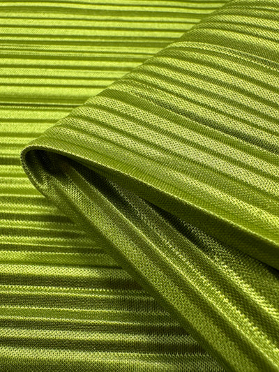 A close-up of the Metallix Pleat in chartreuse showcases its shiny, ribbed texture. This lightweight 140cm polyester fabric from Super Cheap Fabrics features a reflective surface that highlights its intricate horizontal lines and smooth appearance.