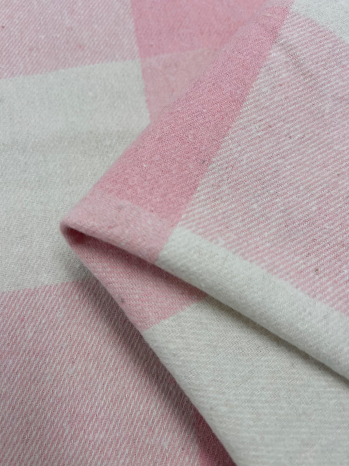 Close-up of the Flannel Plaid - Tickled Pink - 148cm fabric by Super Cheap Fabrics, displaying its heavy weight and checkered pattern in shades of tickled pink and white. The folded fabric highlights its texture and geometric design.