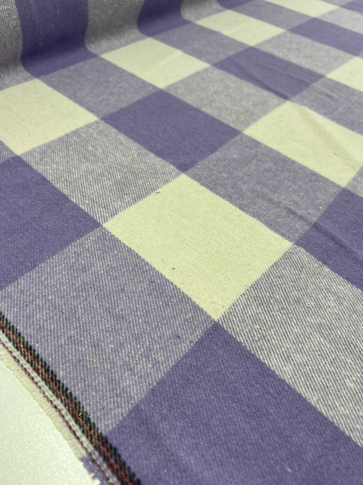 A close-up view of the Super Cheap Fabrics' Flannel Plaid - Viola - 148cm reveals a heavyweight fabric with a checkered pattern. This design features alternating squares of viola and off-white, showcasing its soft texture and well-woven polyester material.