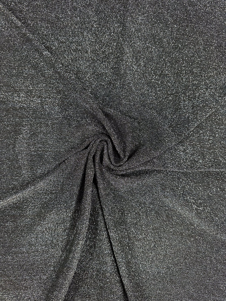 A detailed view showcases the Metallic Lycra - Silver - 160cm from Super Cheap Fabrics, highlighting its shimmering dark gray texture. Perfect for crafting tops or dresses, the fabric is elegantly displayed in a spiral arrangement with folds radiating outwards from the center.