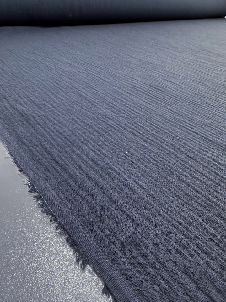 Close-up of a Super Cheap Fabrics Muslin - Navy - 135cm, featuring textured horizontal ridges and laid flat. The slightly frayed edges emphasize the material's softness and depth.