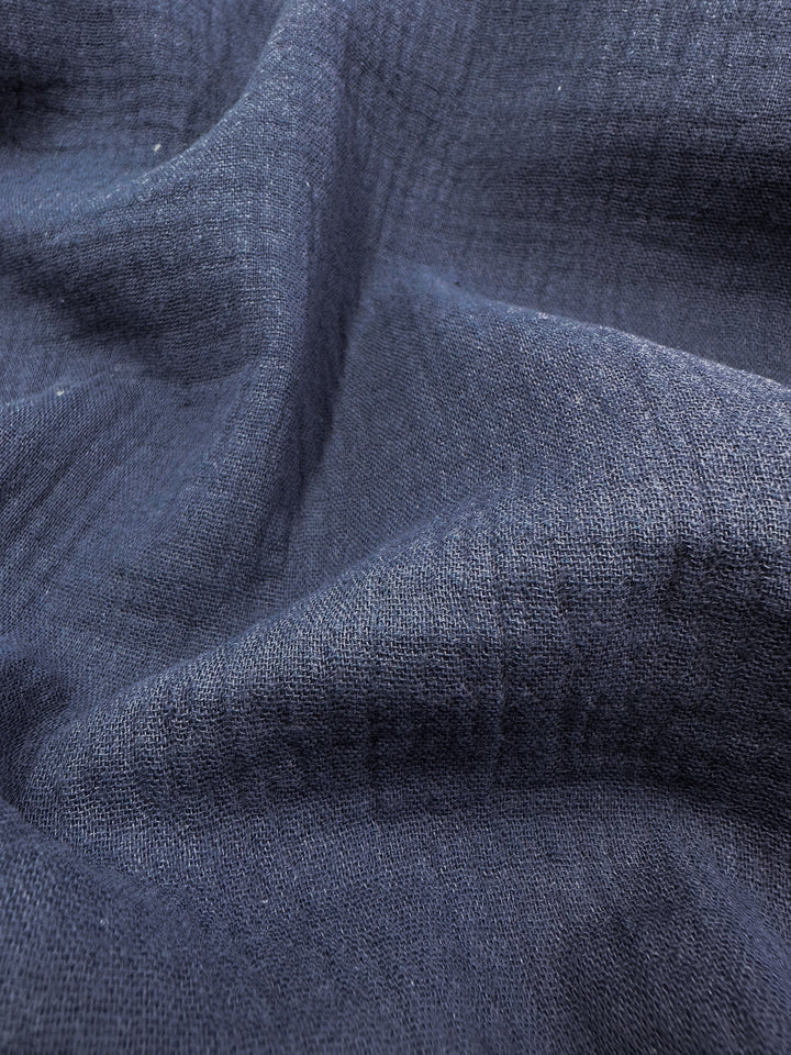 Close-up image of Super Cheap Fabrics' Muslin in Navy, showcasing its dark, textured organic fabric with gentle folds and a soft, woven appearance. The material is 135cm wide and appears thick and durable, featuring subtle variations in shading.