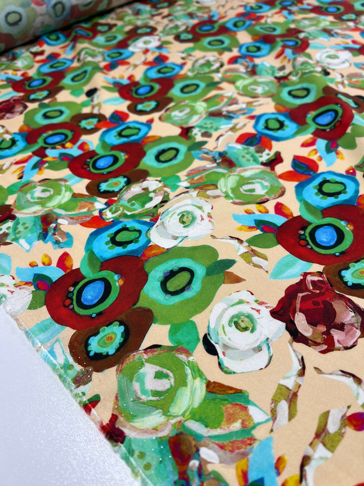 A close-up image of the versatile Super Cheap Fabrics' Designer Rayon - Eloise - 145cm fabric spread out on a surface. This lively and artistic choice features colorful, abstract flowers in shades of green, red, blue, and white on a beige background.