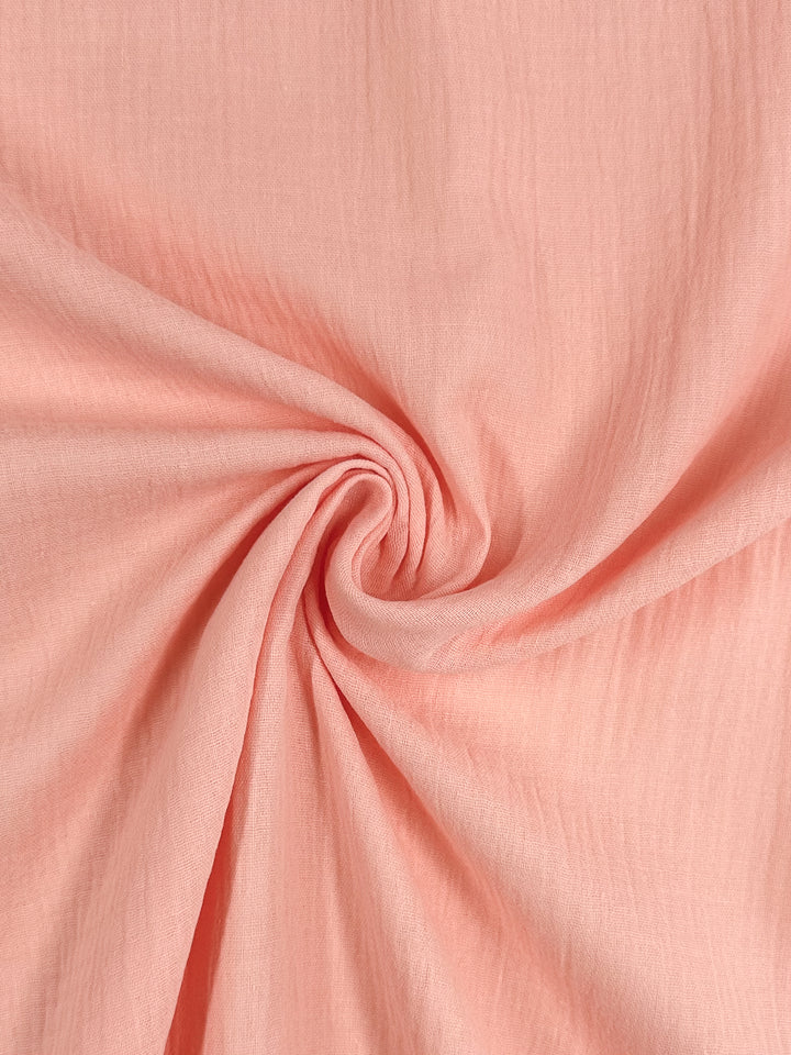 Close-up of the "Muslin - Peach Parfait - 135cm," a product by Super Cheap Fabrics, featuring a spiral pleat design in the center, which highlights the texture and hue of this luxurious organic material.