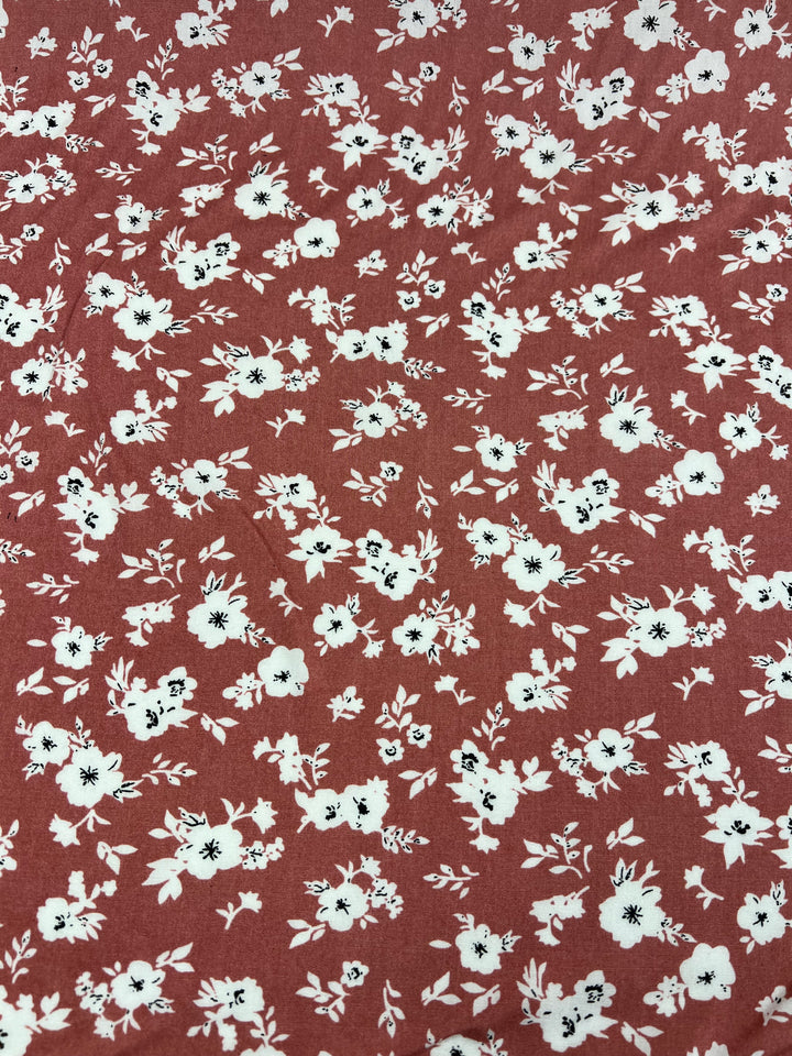 A vibrant print of small white and black flowers on a red background, beautifully scattered to create a balanced and intricate design. The "Printed Rayon - Mona Lisa - 145cm" from Super Cheap Fabrics is a multi-use fabric perfect for various creative projects.