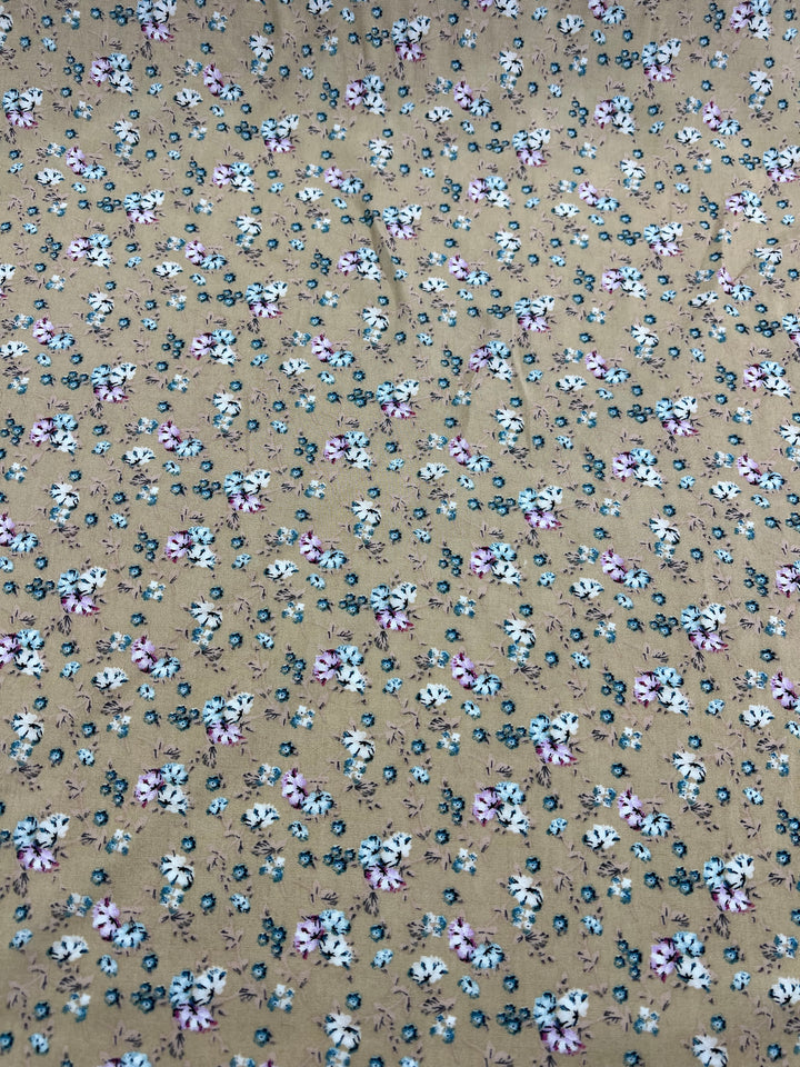 This versatile choice from Super Cheap Fabrics, the Printed Rayon - Pansy - 145cm, features a beige background adorned with a dense and scattered pattern of small white, pink, and blue flowers accompanied by green leaves. The vibrant prints are evenly spread across the entire surface.