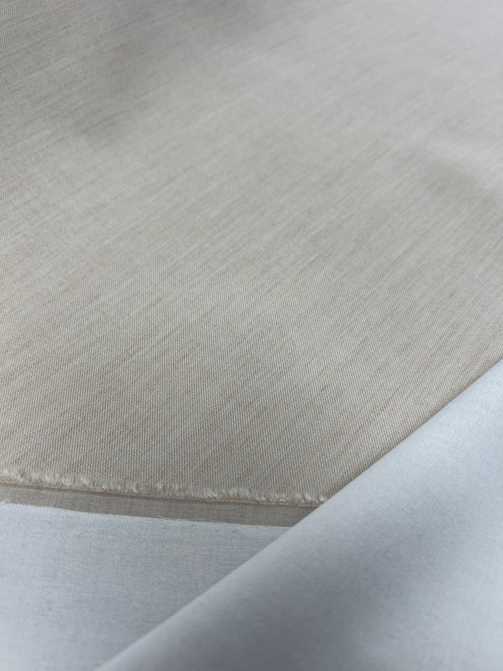 Close-up of the Designer Suiting - Sandy from Super Cheap Fabrics, showcasing a smooth, sand-colored Polyester fabric with a slightly visible weave pattern. The edges of the medium to heavy weight suiting layers are shown, providing a subtle contrast between the different shades of beige and white.