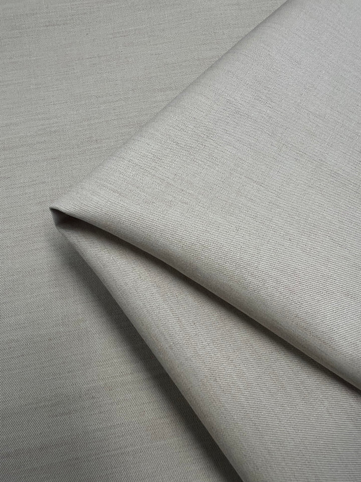 A close-up of the neatly folded Designer Suiting - Sandy - 150cm from Super Cheap Fabrics, highlighting its light gray hue and medium to heavy weight. The polyester fabric presents a smooth yet slightly textured surface, showcasing its fine weave and subtle sheen.