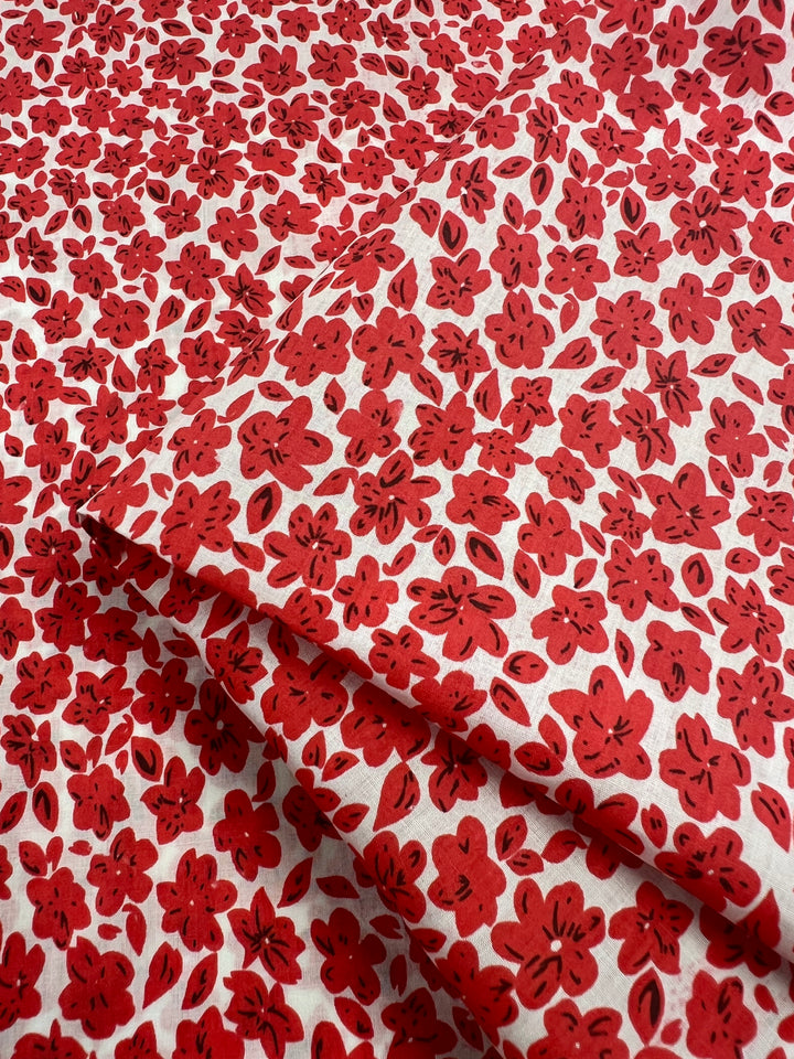 A folded 100% cotton fabric known as "Printed Cotton - Red Rain - 145cm" from Super Cheap Fabrics, featuring a vibrant pattern of red flowers with black accents on a white background. The dense floral design covers the entire surface of this lightweight, printed cotton fabric.