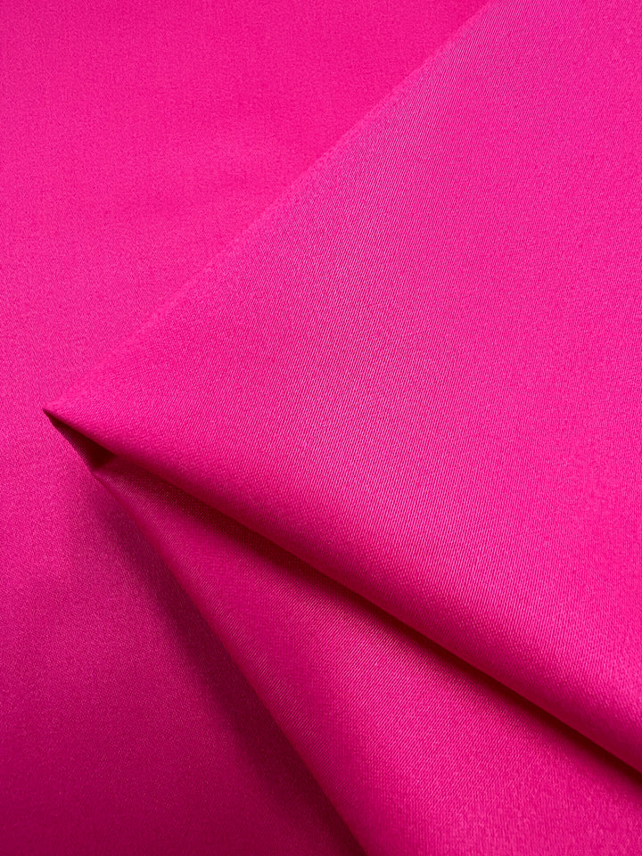 Close-up of Super Cheap Fabrics' Plain Sateen - Hot Pink - 140cm reveals its vibrant color and smooth texture, with subtle folds showing sheen and depth.