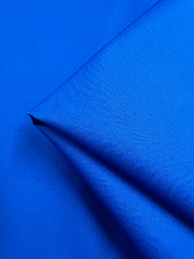 A close-up of Super Cheap Fabrics' Plain Sateen - Royal - 140cm displays its vibrant royal blue color and smooth texture. The neatly folded fabric showcases its richness and quality, perfect for clothing and décor.