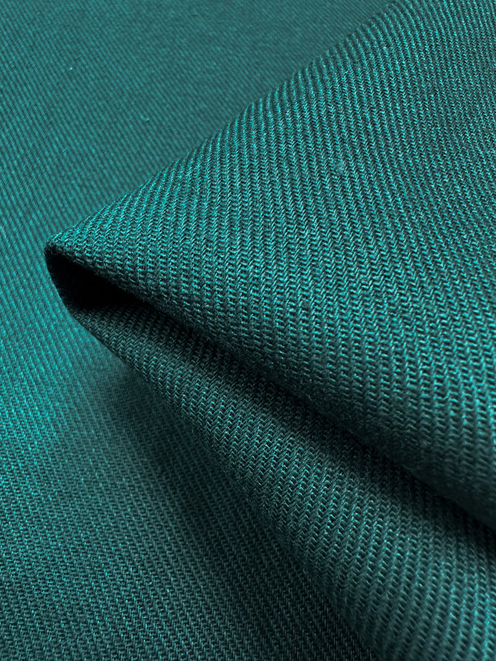 Close-up of the Pure Washed Linen - Jasper from Super Cheap Fabrics, displaying its folded dark green fabric with a ribbed texture. The fine weave and smooth surface are accentuated by lighting that highlights the subtle sheen and detailed pattern of this lightweight fabric, meticulously crafted from pure linen.