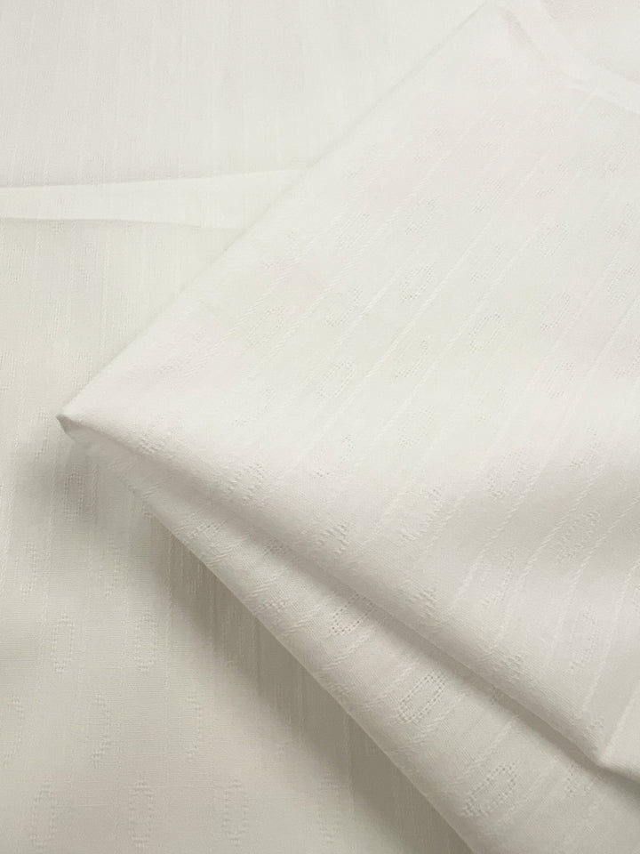 Close-up of Super Cheap Fabrics' Textured Cotton - White - 145cm, showcasing its delicate and lightweight nature. The image captures the 100% cotton fabric neatly folded and arranged on a flat surface, displaying its subtle, textured pattern. The material appears slightly translucent, indicating its soft and smooth texture.