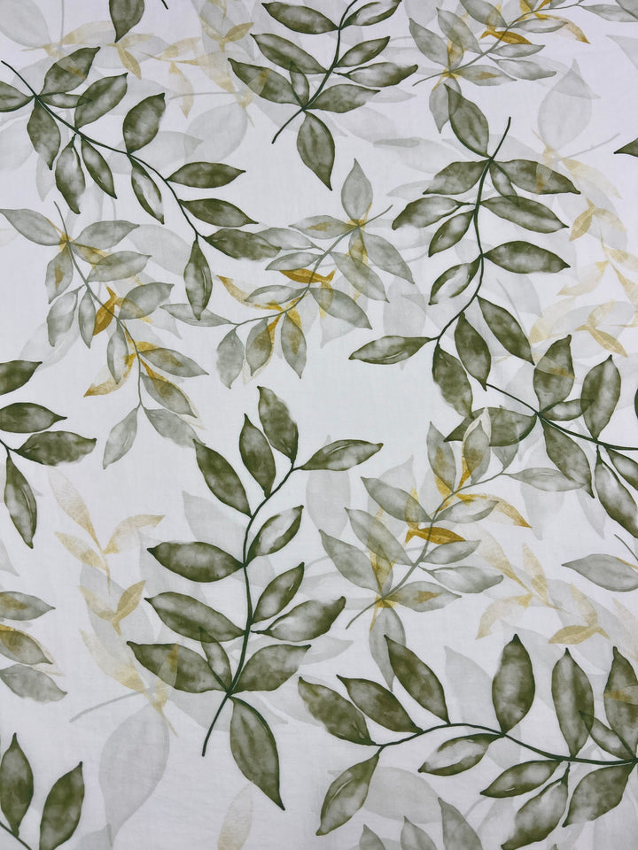 **Designer Cotton - Gully - 150cm** by **Super Cheap Fabrics** is a lightweight cotton fabric featuring a white background adorned with an elegant pattern of leafy designs in various shades of green with hints of yellow. The leaves are arranged in a scattered yet orderly manner, making this fabric ideal for luxury sewing projects and achieving a natural, organic look.