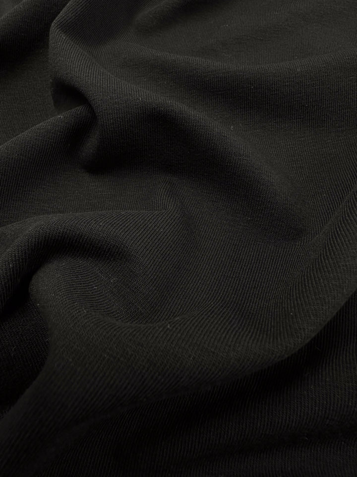 A close-up of the breathable black fabric, Cotton Lycra - Black - 190cm by Super Cheap Fabrics, reveals its smooth texture and gentle folds with soft shadows and highlights, ideal for crafting sleek bodycon dresses.