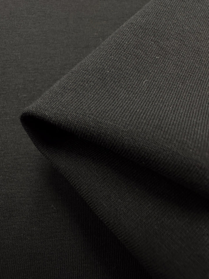 A close-up shows a folded piece of medium-to-heavy weight Cotton Lycra fabric, known for its smooth texture and fine weave. This dense, slightly glossy material from Super Cheap Fabrics is ideal for clothing or textiles due to its breathable knit.