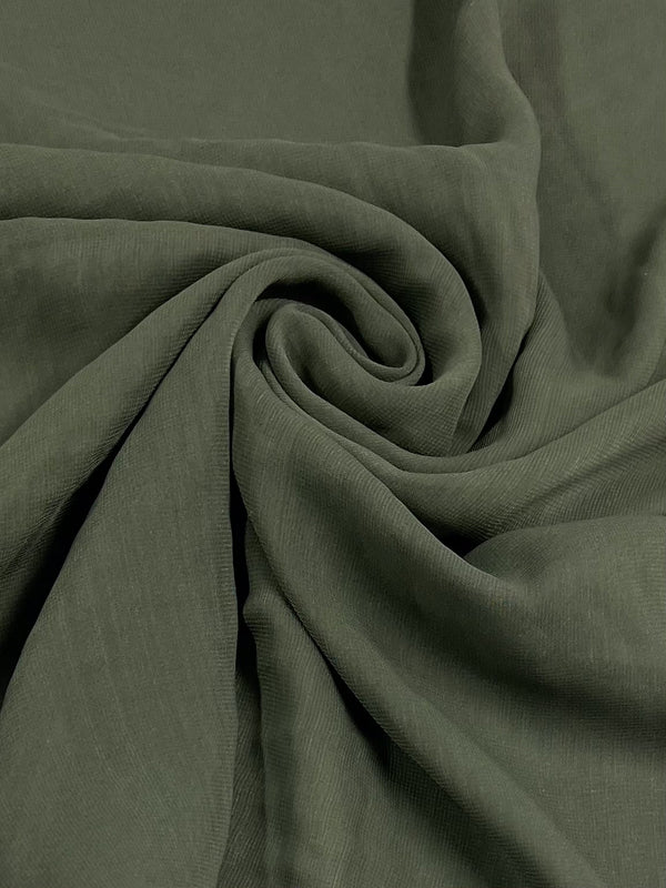 The Hi-Multi Chiffon in Dusty Olive from Super Cheap Fabrics features a lightweight, green fabric with a slightly wrinkled texture, arranged in a spiral pattern at the center for a soft and flowing appearance, ideal for creating floaty tops.