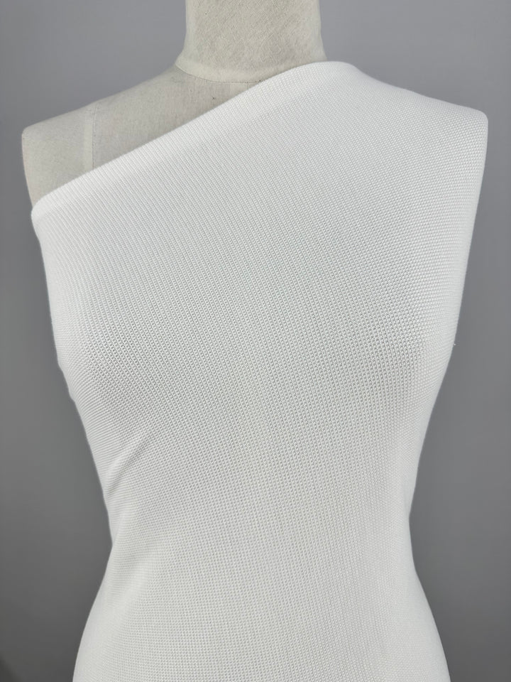 A torso mannequin is dressed in the Honeycomb Knit - Vanilla - 158cm by Super Cheap Fabrics. The background is plain gray, keeping the focus on the clothing. The top has a waffle fabric knit pattern that covers both the chest and waist areas of the mannequin, adding a subtle three-dimensional effect to its design.