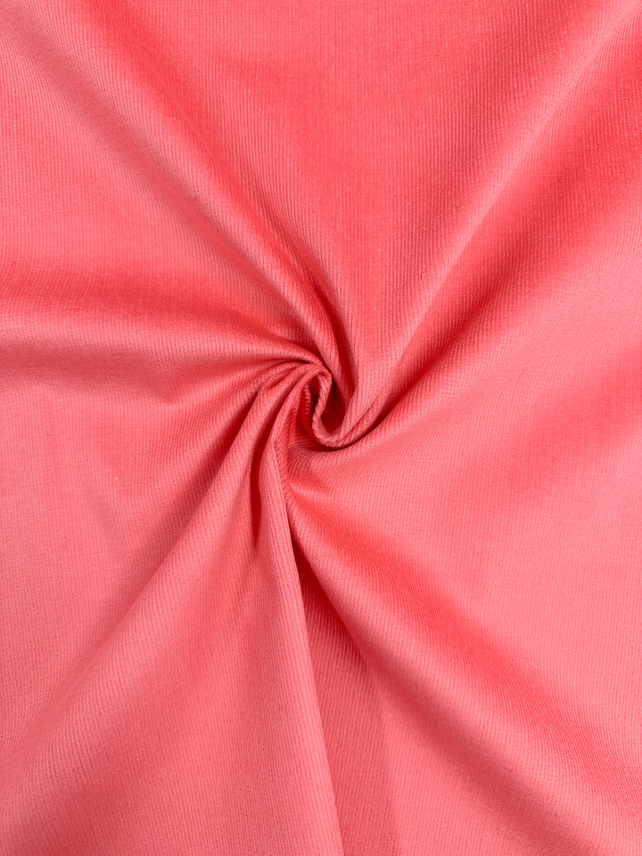 The Micro Wale Corduroy - Dubarry fabric by Super Cheap Fabrics, with its pink sheen and gentle folds twisting at the center, showcases a soft texture and elegant drape that evokes cozy winter clothing.