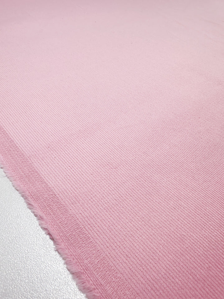 A close-up of Super Cheap Fabrics' Micro Wale Corduroy in Tickled Pink, 142cm wide, highlighting its ribbed weave and frayed left edges. The soft, slightly reflective texture is ideal for winter clothing.