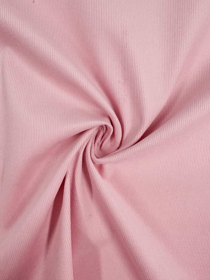 A close-up of the Super Cheap Fabrics' Micro Wale Corduroy - Tickled Pink - 142cm, showcasing its ribbed texture, gathered and twisted into a spiral pattern.