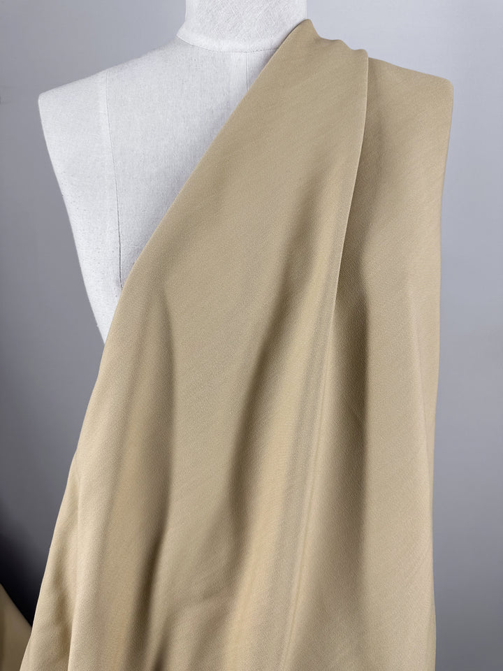 A mannequin showcases the Stretch Viscose Suiting fabric in Pebble from Super Cheap Fabrics. The 130cm wide material has a soft and smooth texture, elegantly draped against a neutral background.