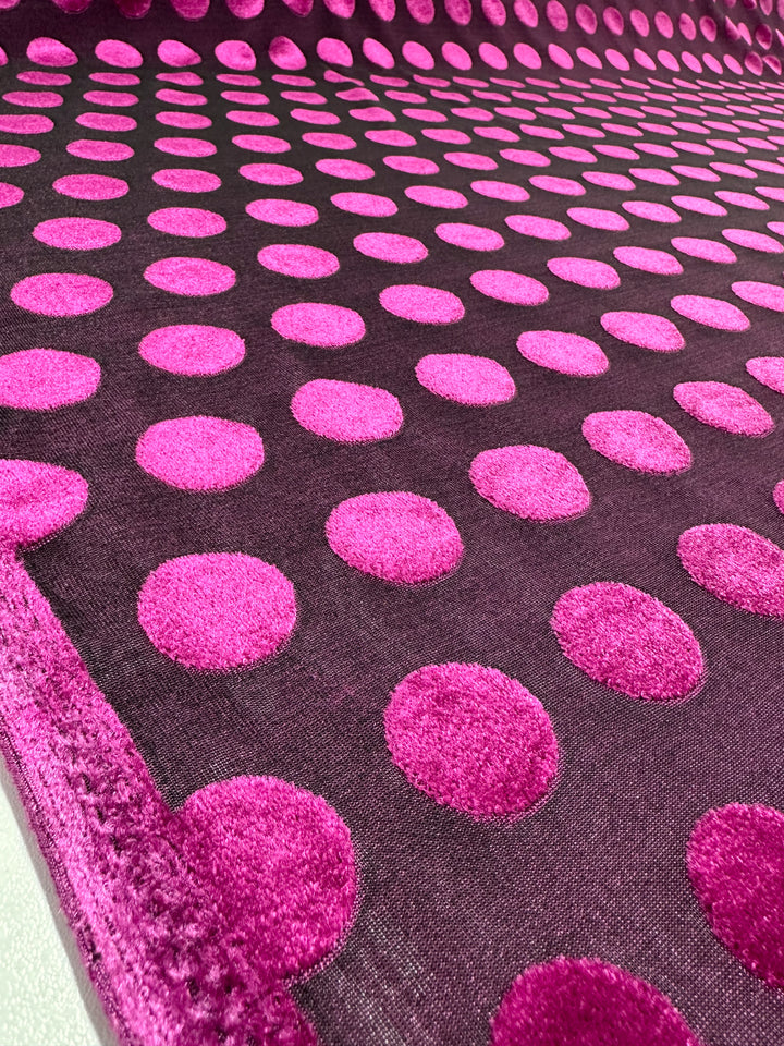 Close-up of Super Cheap Fabrics' Burnout Velvet in Festival Fuchsia, 155cm: a luxurious fabric featuring large pink polka dots on a dark background. The soft, velvety texture creates an exquisite textile art piece with evenly spaced dots.