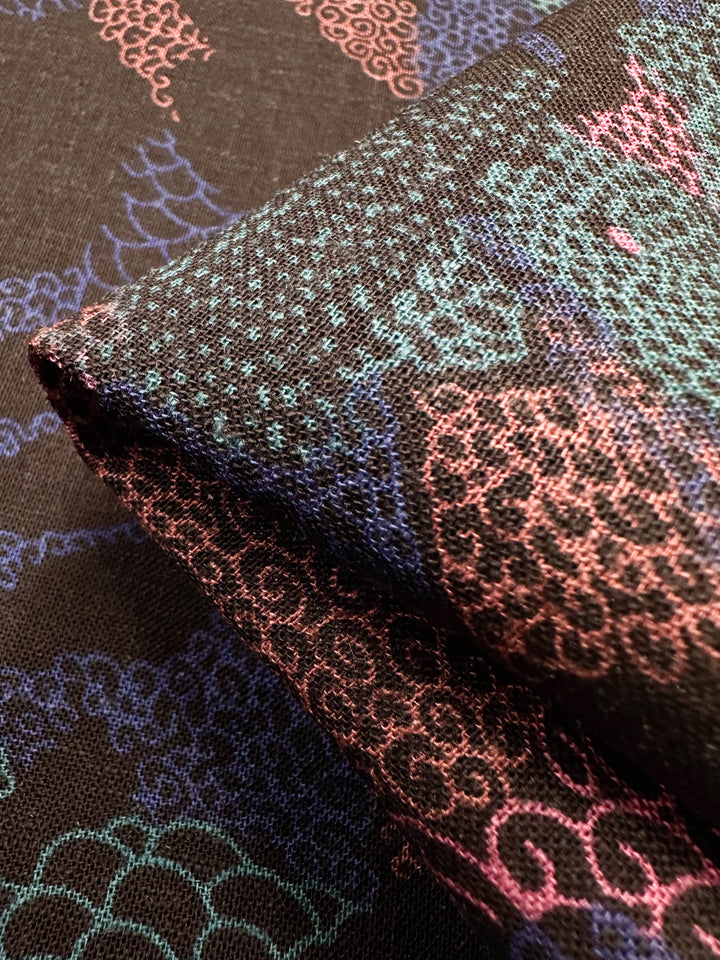 Close-up of folded Linen Blend - Coral - 147cm by Super Cheap Fabrics, featuring intricate pink, blue, and green patterns on a black background with swirling and scale-like motifs in a tapestry-like texture.