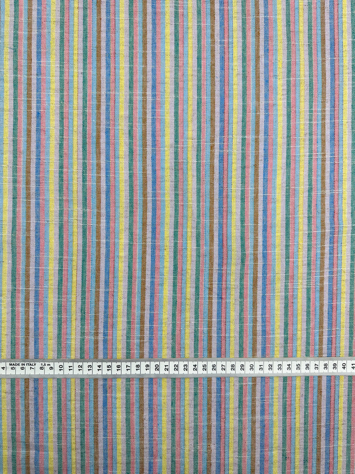 The Linen Blend - Tropicana - 143cm from Super Cheap Fabrics features vertical stripes in blue, pink, yellow, and white on yarn-dyed linen for a vintage charm. Measurements are shown in centimeters with a ruler at the bottom.