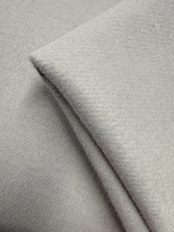 A close-up of Super Cheap Fabrics' Wool Cashmere - Windchime (150cm) shows its soft, light grey material neatly folded. The fuzzy texture highlights its cozy warmth—ideal for elegant, luxurious creations.