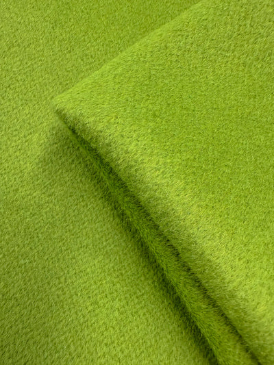 A close-up of Super Cheap Fabrics' Wool Cashmere - Titanite (154cm): textured, bright green heavyweight wool with a slightly fuzzy, luxuriously soft surface and a visible folded edge.