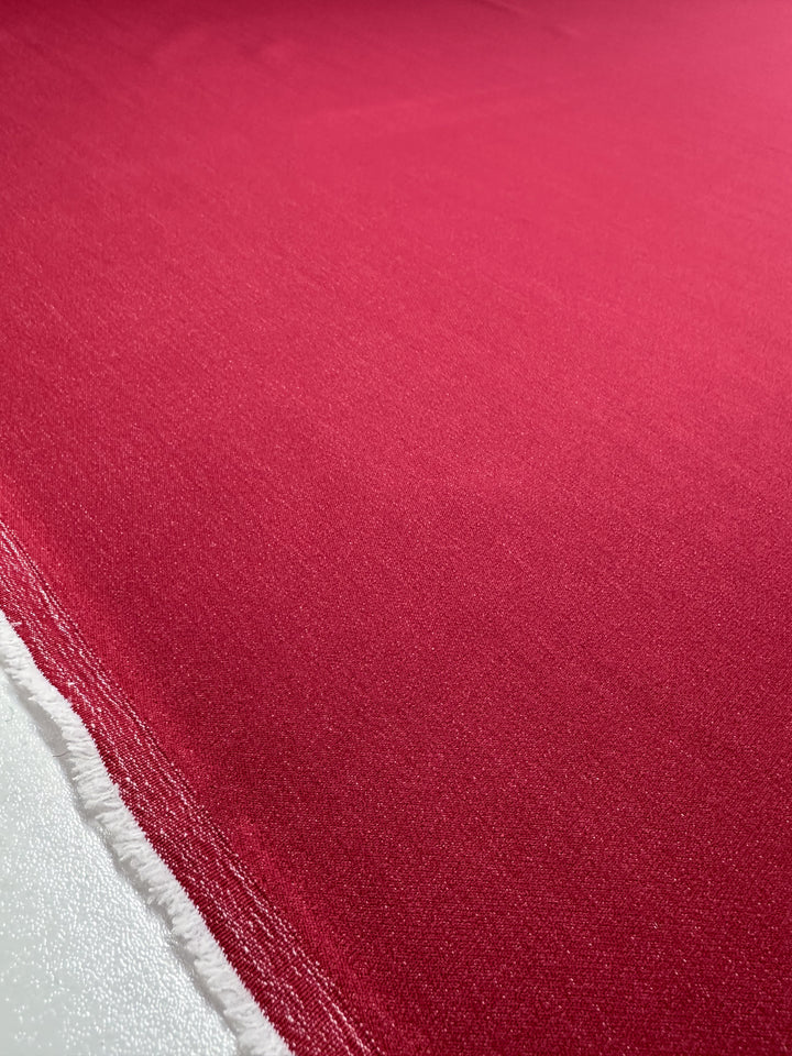 A close-up shows the textured weave of Super Cheap Fabrics' Stretch Denim - Scooter - 145cm. Red fabric with frayed edges reveals white threads, while the surface's light reflection highlights its smooth, high-quality texture.