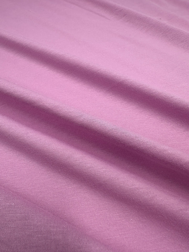 A close-up of Super Cheap Fabrics' Cotton Jersey in Pastel Lavender, 160cm wide, shows smooth, slightly velvety fabric with horizontal folds casting subtle shadows.