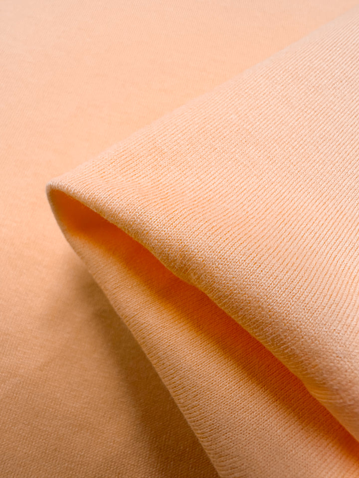 A close-up of the folded Cotton Jersey - Papaya from Super Cheap Fabrics reveals its medium weight texture and weave. Made of cotton, this 160cm wide jersey is soft, slightly stretchy, and reminiscent of ripe papaya with its fine knit.