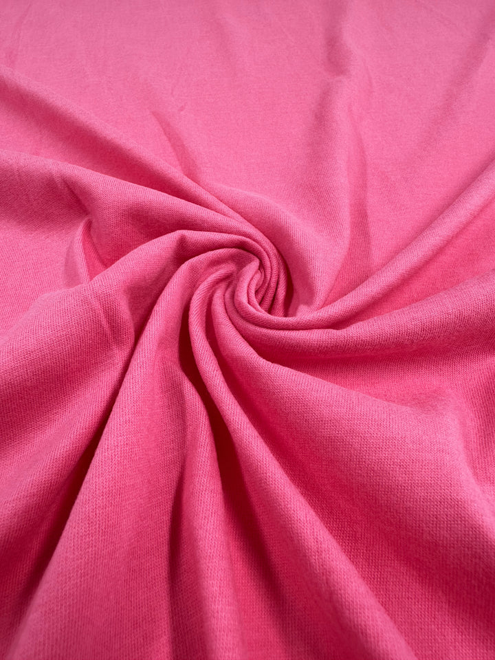 A close-up of Super Cheap Fabrics' Cotton Jersey in Fandango Pink (160cm) reveals a central swirl pattern. The soft, smooth cotton texture creates a dynamic visual effect resembling a spiral.