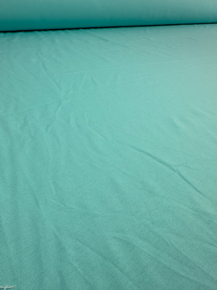 A close-up of Super Cheap Fabrics' Cotton Jersey in Aqua Splash, 160cm wide, reveals its smooth turquoise surface with subtle wrinkles and texture.