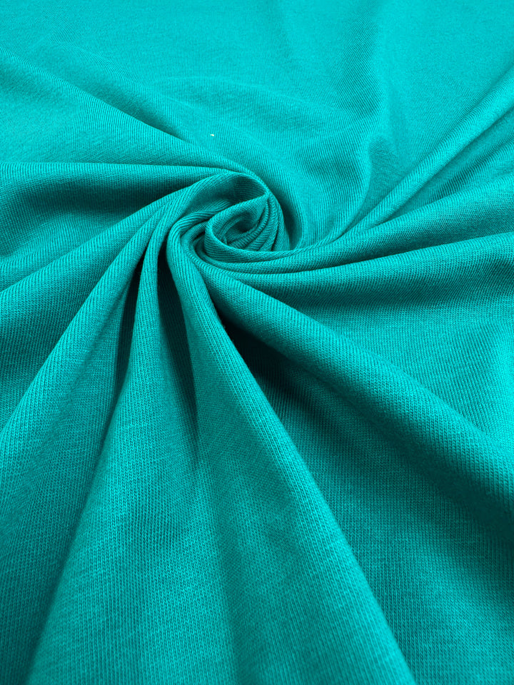 A close-up image of the Cotton Jersey - Kayaking fabric by Super Cheap Fabrics, showcasing its teal color intertwined into a spiral, highlighting the soft folds and texture.