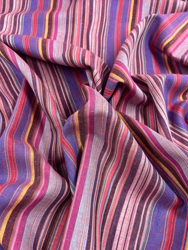 A close-up of the Linen Blend - Goa - 150cm by Super Cheap Fabrics highlights its vibrant vintage look, featuring vertical stripes in shades of pink, purple, orange, and blue. The yarn-dyed texture appears soft and seamlessly blends colors to create a dynamic and colorful pattern.