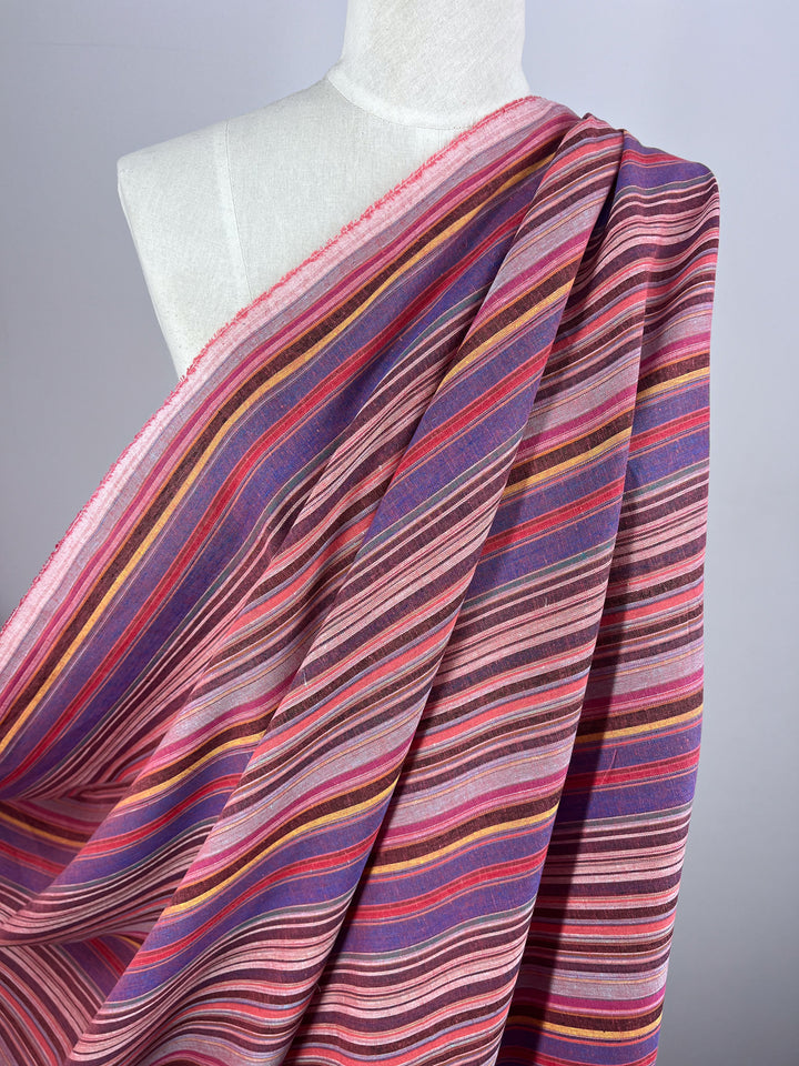 A mannequin adorned with the Linen Blend - Goa - 150cm fabric from Super Cheap Fabrics, showcasing a vibrant pattern of horizontal stripes in pink, purple, orange, and red hues. The vintage charm is highlighted by its textured design against the mannequin's plain white surface.