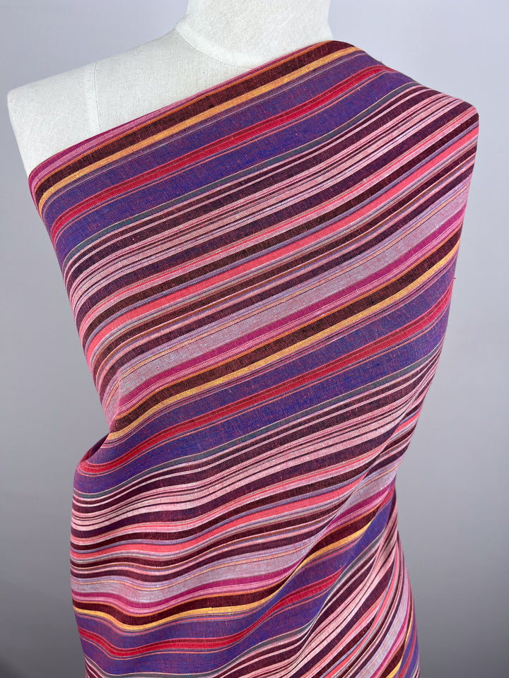 Close-up of a mannequin adorned with the "Linen Blend - Goa - 150cm" fabric by Super Cheap Fabrics, showcasing vibrant stripes in pink, purple, red, orange, and blue. The varied thickness of the stripes creates an eye-catching vintage pattern against a plain light gray background.