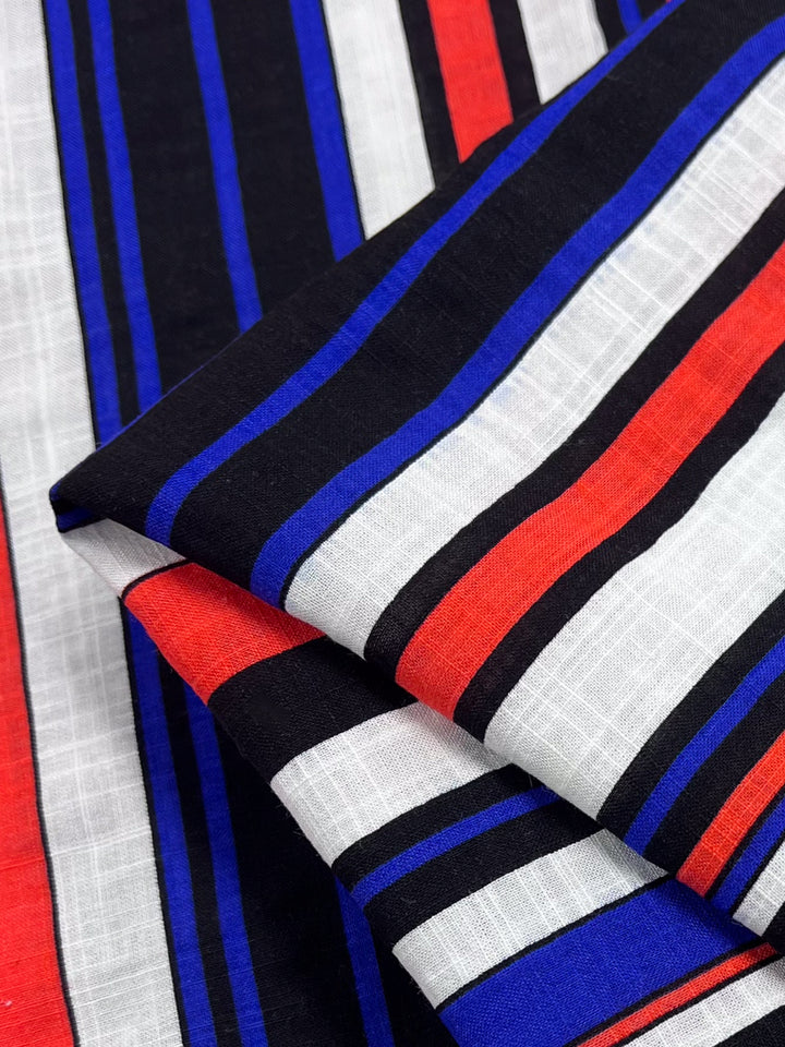 Close-up of Super Cheap Fabrics' "Linen Blend - Minimal - 145cm" highlighting its lightweight composition with black, red, blue, and white vertical stripes. The breathable linen blend is folded to show multiple layers with diverse stripe patterns, creating a textured appearance.