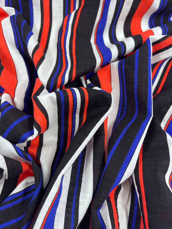 Product Description: The Linen Blend - Minimal - 145cm by Super Cheap Fabrics is a lightweight linen blend that features bold vertical stripes in red, black, blue, and white. This breathable material has a soft feel and a slightly crumpled texture, with intersecting stripes of varying thickness.