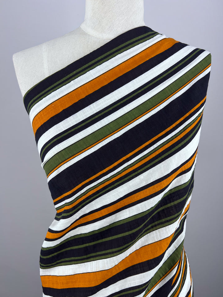 The Linen Blend - Retro - 145cm by Super Cheap Fabrics, showcasing diagonal stripes in black, white, orange, and dark green on a light grey backdrop, is ideal for crafting summer outfits with its breathable quality.