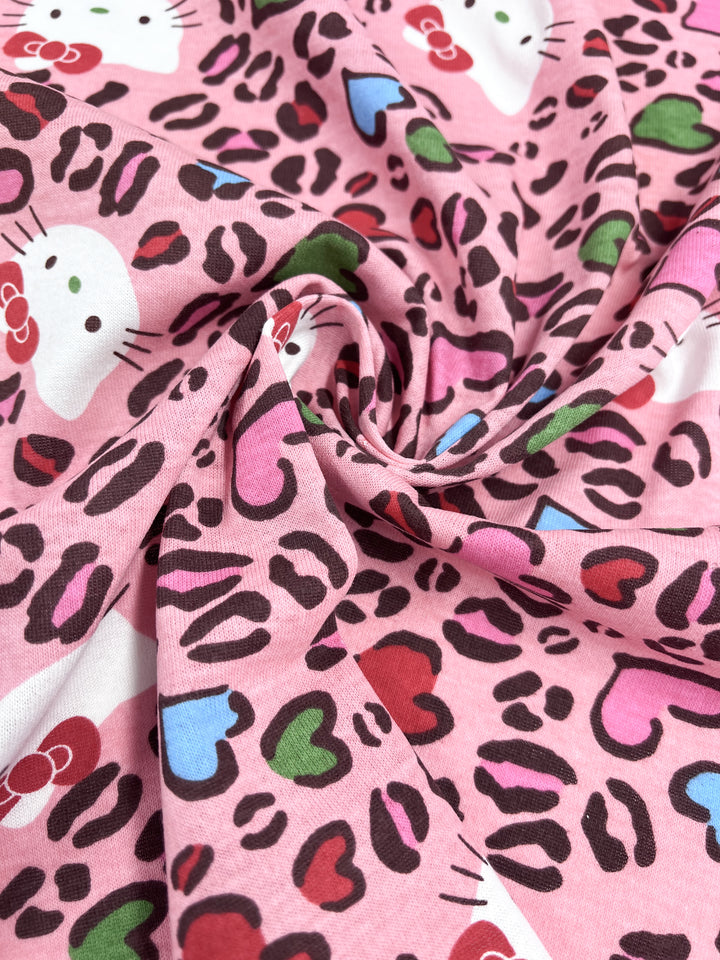 The Super Cheap Fabrics Printed Jersey - Hello - 150cm is a lightweight fabric featuring a swirl pattern with leopard spots, colorful hearts in blue, red, and green, and cartoon cat faces decorated with red bows.