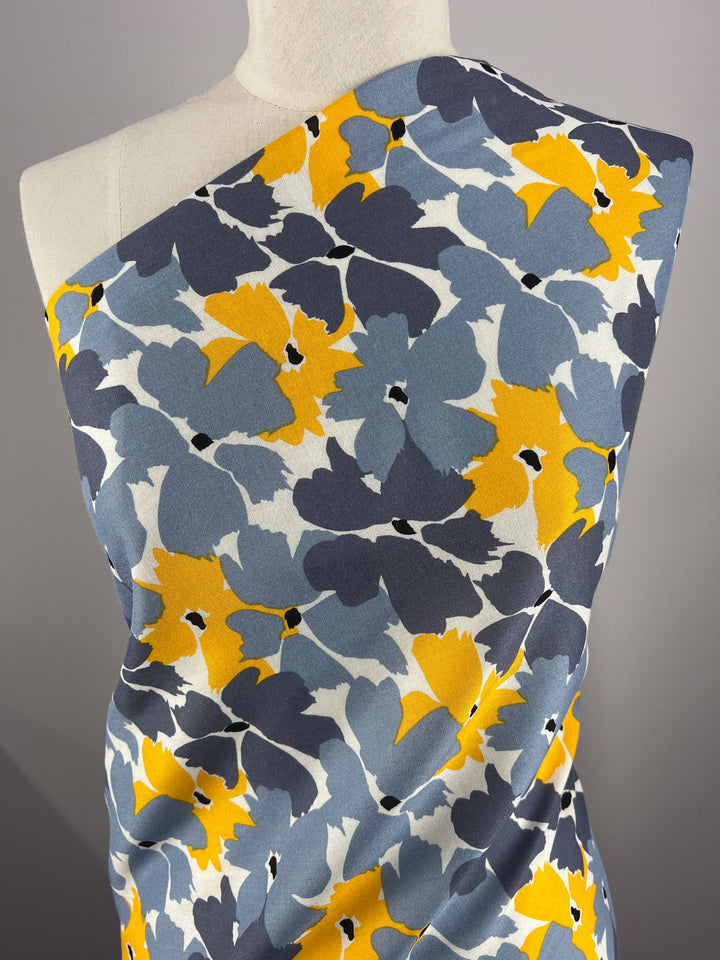 Close-up of the Designer Rayon - Summer - 140cm fabric by Super Cheap Fabrics, draped over a mannequin with bold blue, yellow, and white floral prints on a gray background.