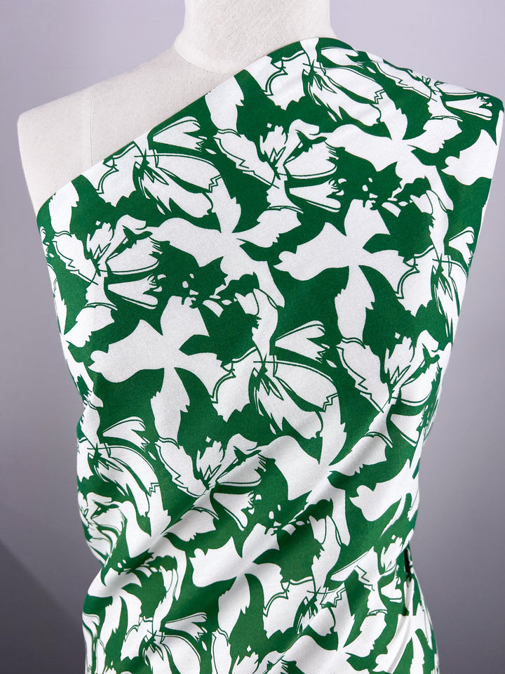 On display is the Designer Rayon - First Tee by Super Cheap Fabrics, a versatile 140cm wide fabric in white and green with bold, abstract floral prints of large stylized flowers and leaves for a striking visual contrast.