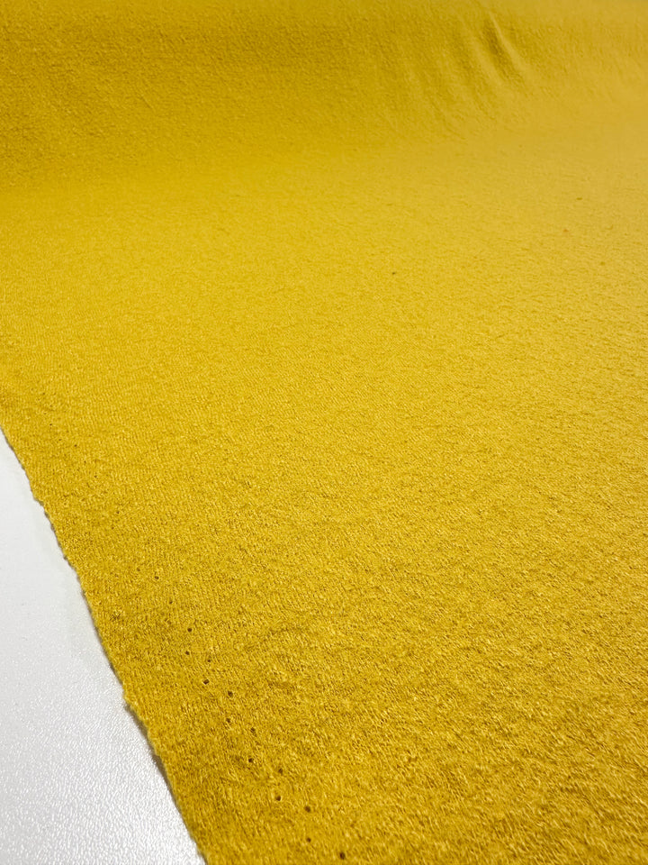 A detailed view of Boiled Wool - Hot Spot - 145cm fabric by Super Cheap Fabrics shows its heavy-weight yellow texture on a white surface, with gentle folds creating shadows and light.