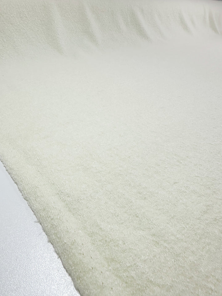 A close-up view of Boiled Wool in Ivory by Super Cheap Fabrics, measuring 150cm, reveals its smooth, fleece-like texture spread across a surface.